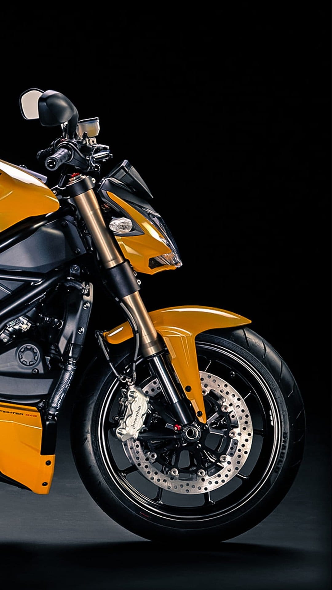 Yellow Ducati motorcycle front wheel featuring a perforated disc brake and golden suspension forks on a dark backdrop.