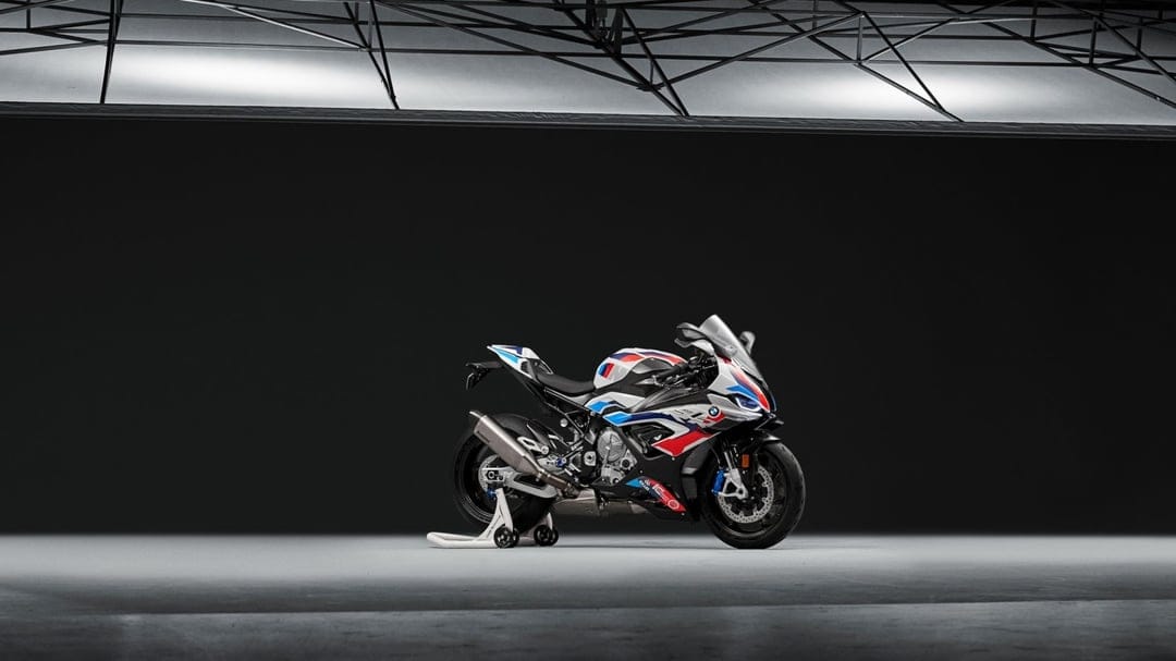 BMW M1000RR sport motorcycle with white, blue, and red livery on a racing stand in a minimalist dark studio.