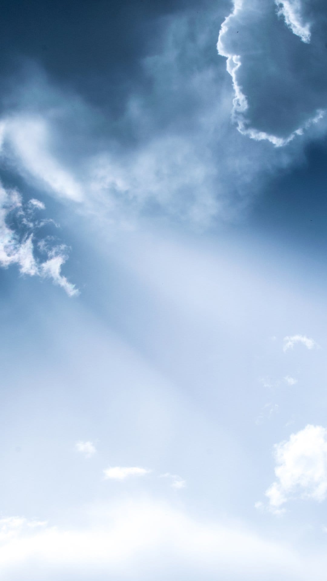 Radiant golden sunbeams piercing through dark, heavy storm clouds against a clear blue sky during a sunshower.