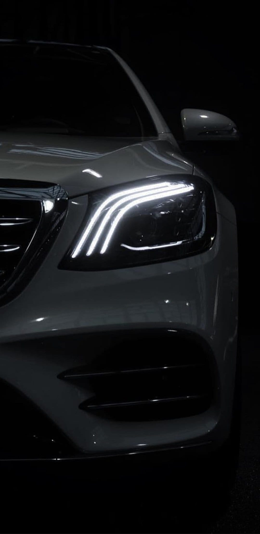 White luxury car headlight with glowing LED daytime running lights against a dark, minimalist background.