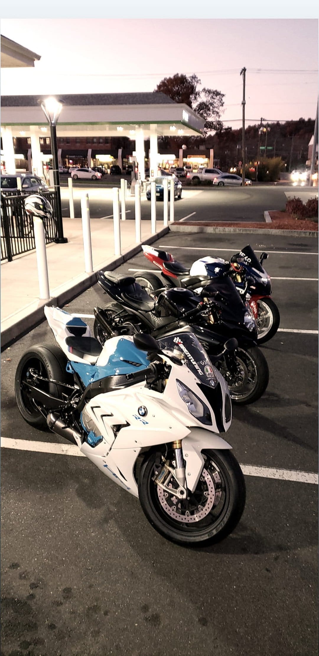 BMW S1000RR and sport motorcycles parked at a lit gas station at night, featuring sharp fairings and neon glow.