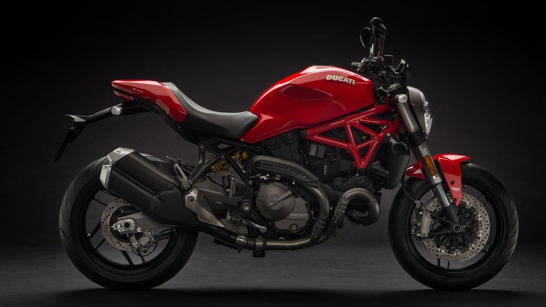 Profile of a red Ducati Monster motorcycle against a black background featuring a trellis frame and studio lighting.