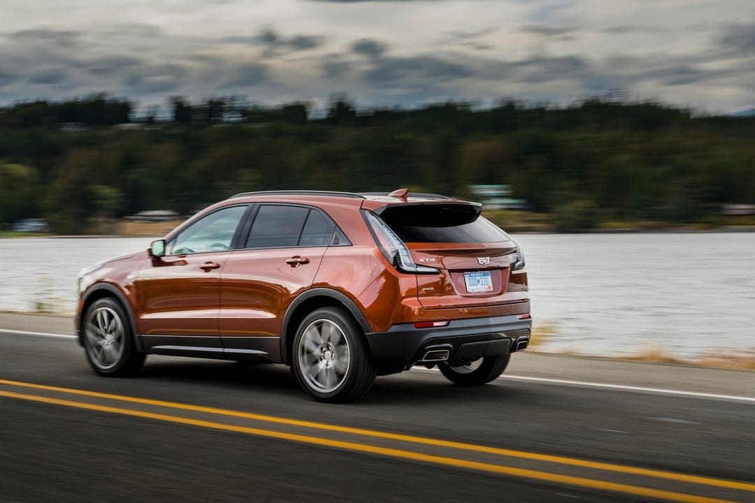 Copper Cadillac XT4 luxury SUV driving fast on a scenic coastal road with motion blur and water in the background