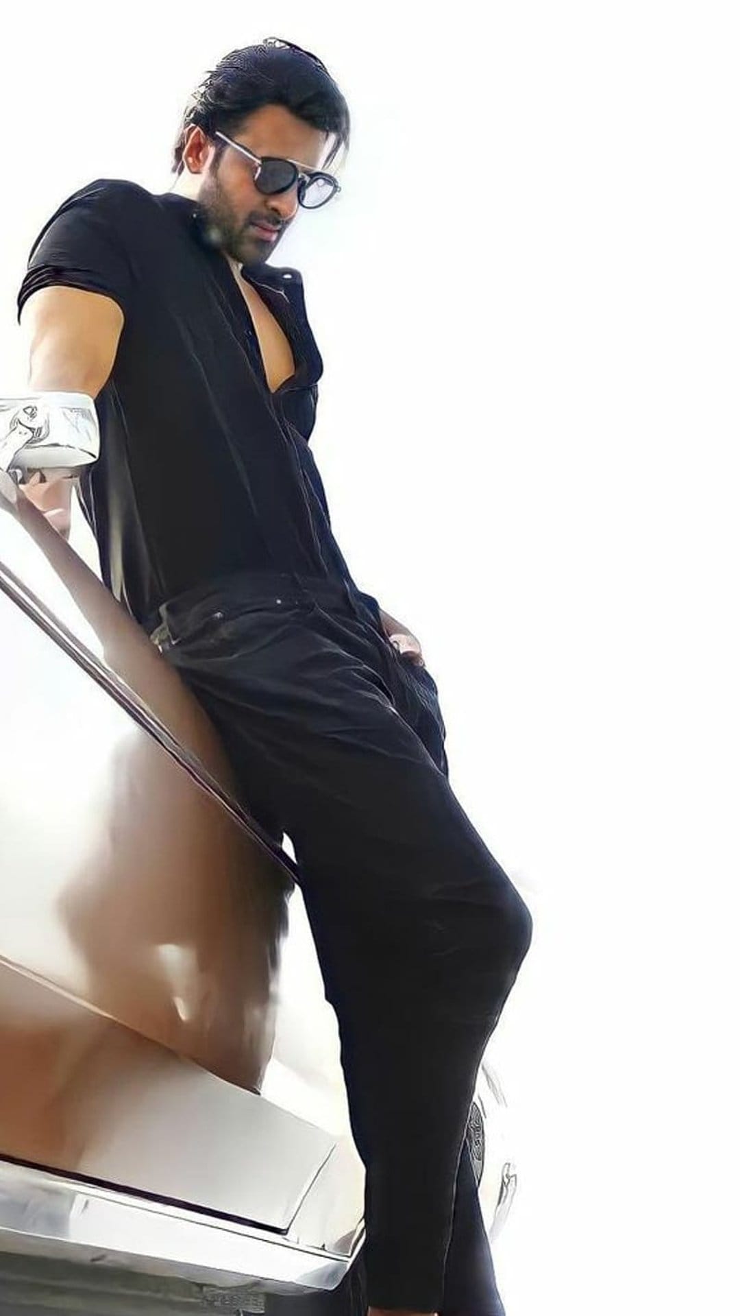 Stylish man in black clothing and sunglasses leans against a car side against a bright high-contrast background.