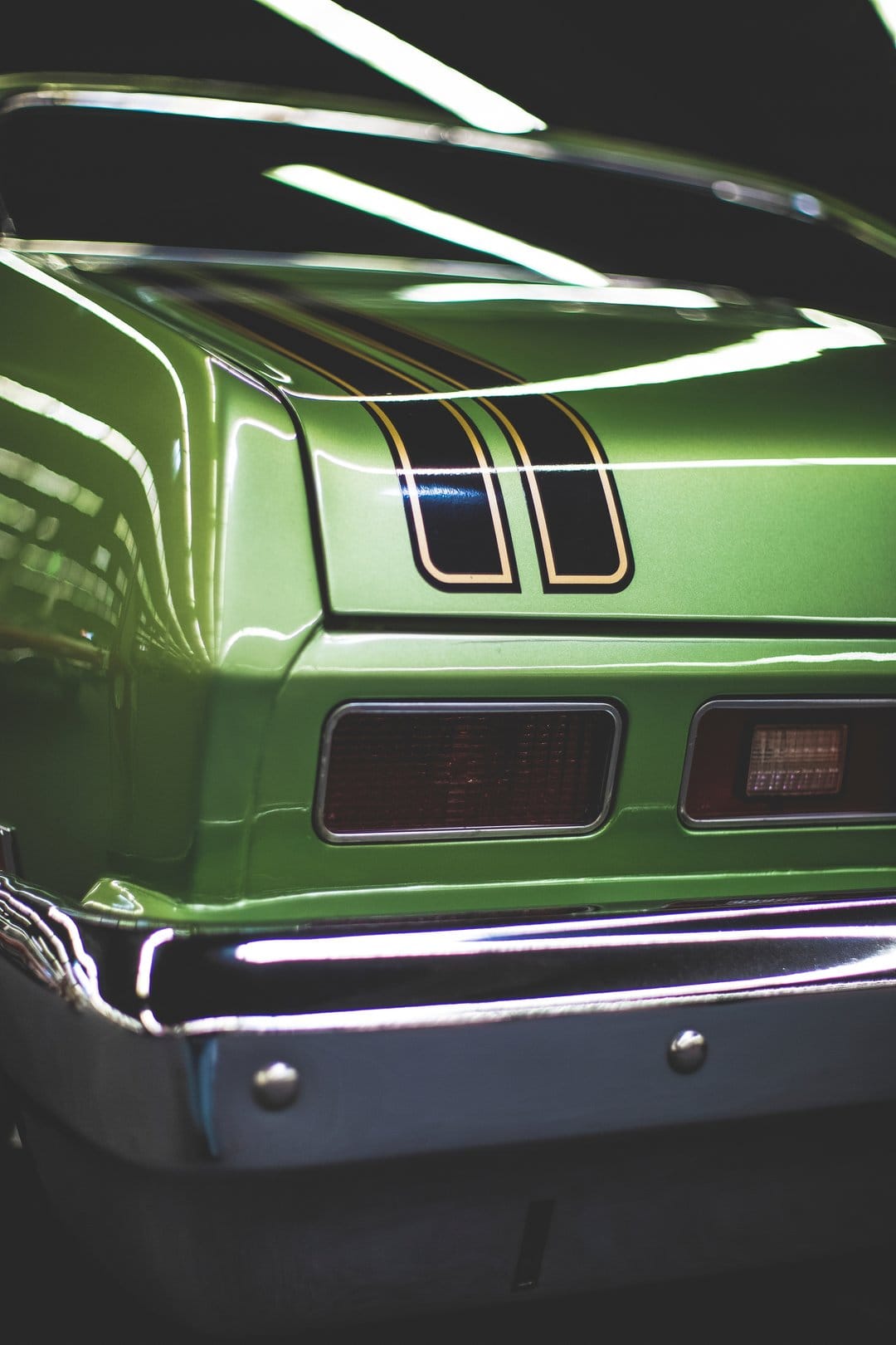 Green classic car rear with black and gold racing stripes, polished chrome bumper, and glowing red taillights.