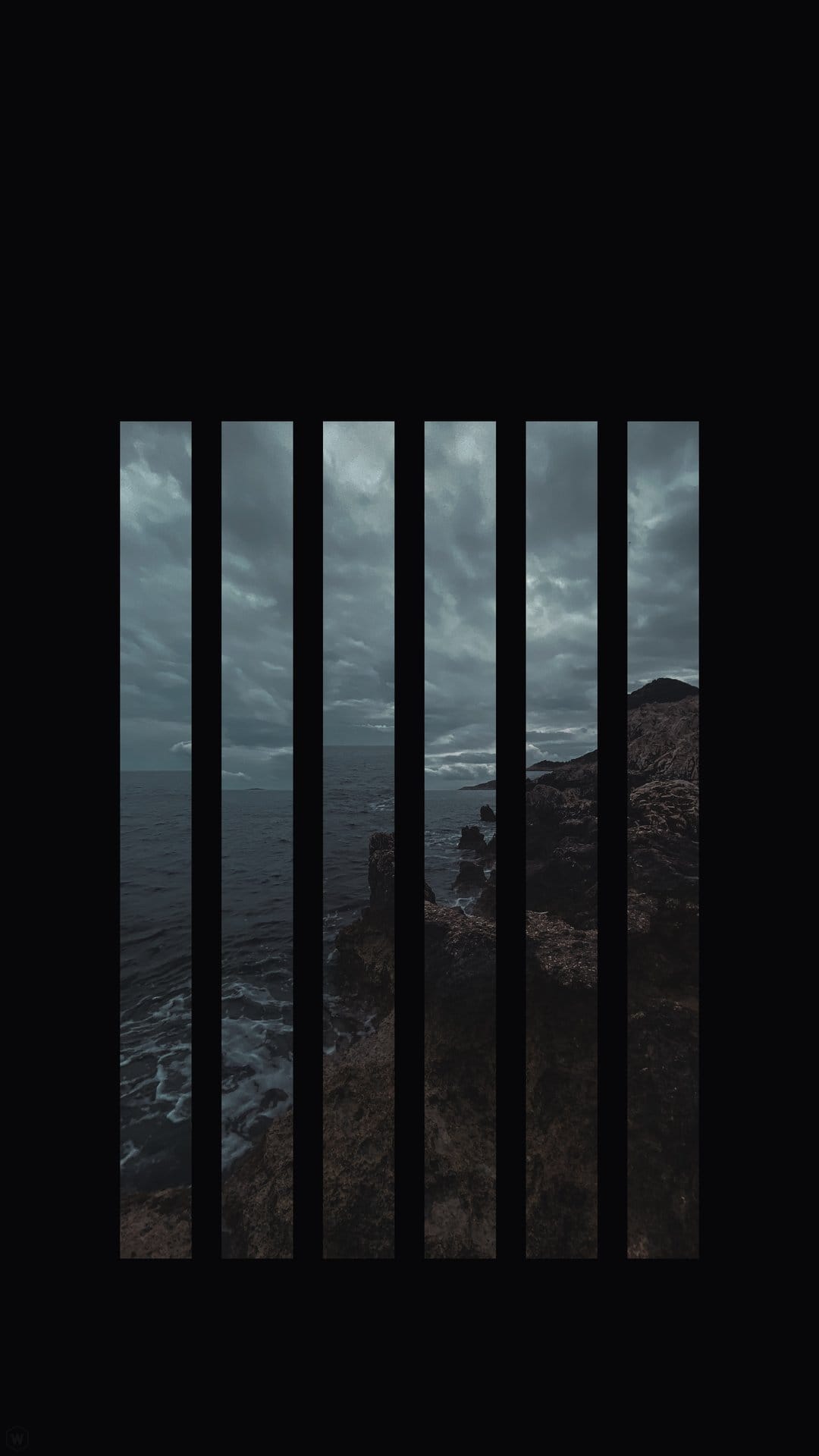 Turbulent grey ocean waves crashing on dark rocks viewed through a series of thick black vertical metal bars.