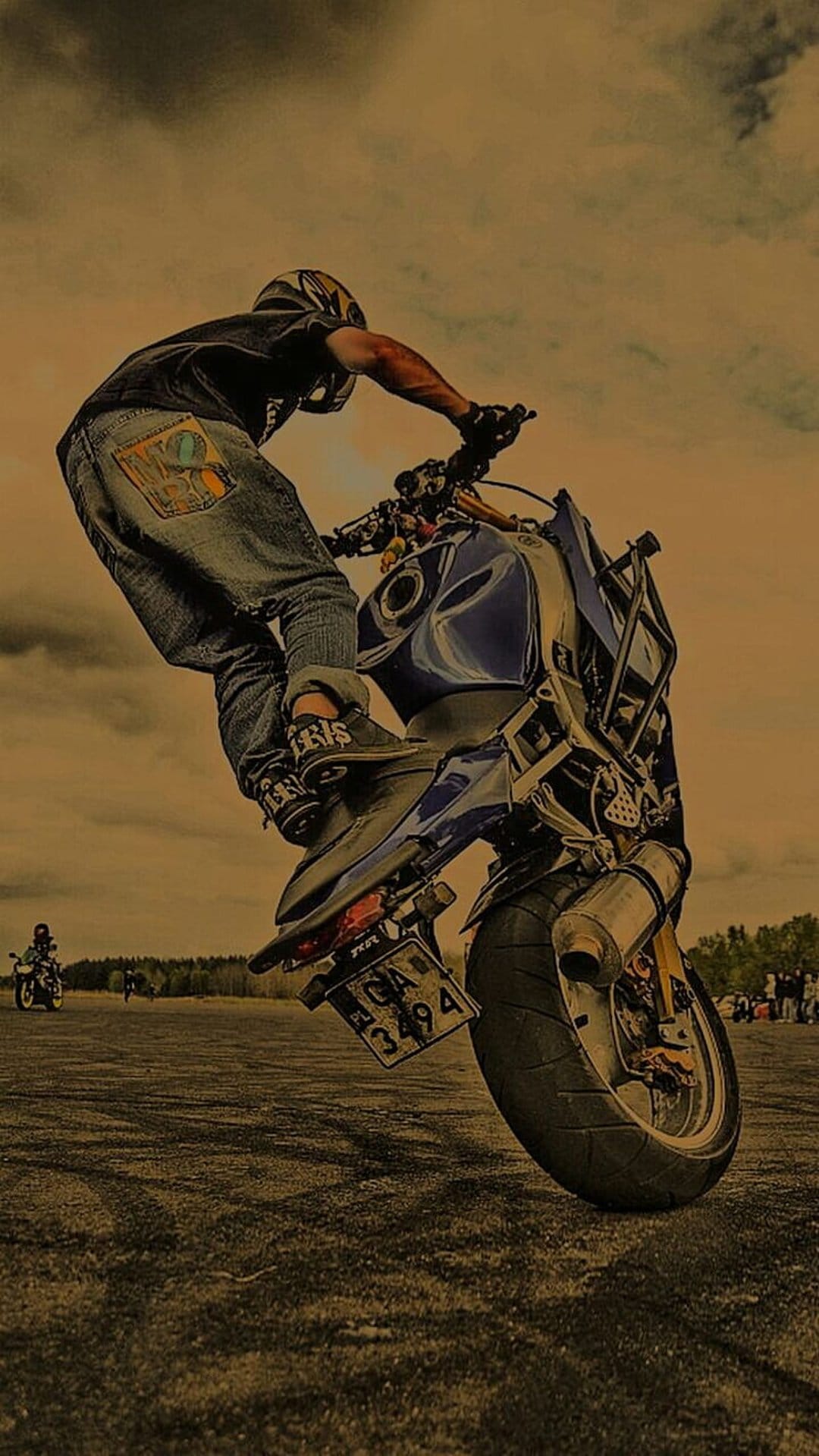 Motorcycle rider performing a vertical wheelie on a flat asphalt lot under a cloudy sky during an outdoor event.