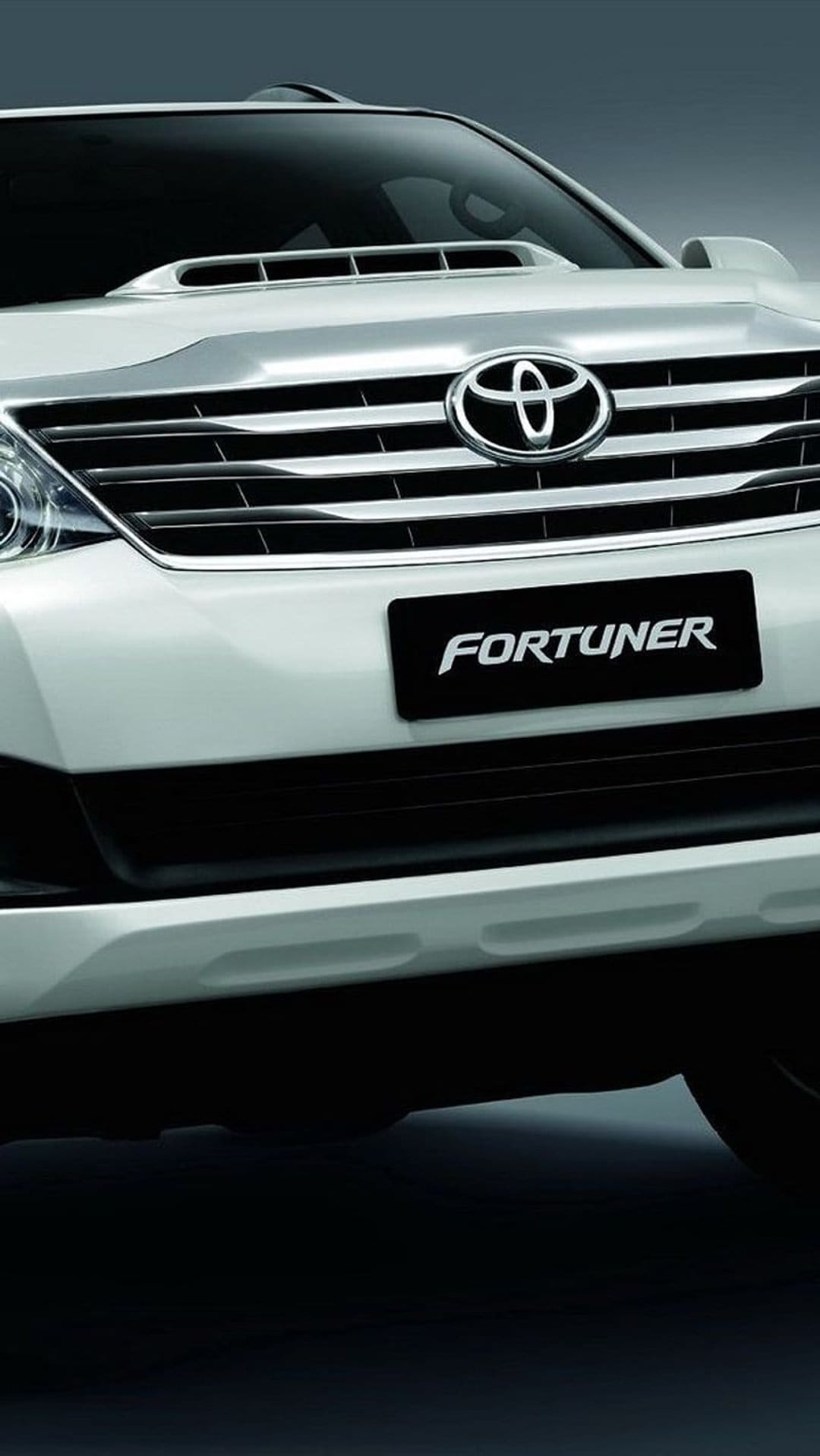 Toyota Fortuner front grille and silver emblem with white bodywork and bold lettering in a vertical car close-up.