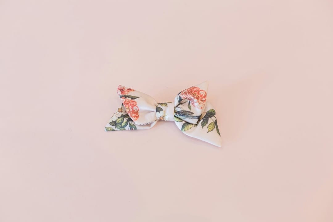 White satin bow with a pink rose pattern and green leaves centered on a solid light pink background.