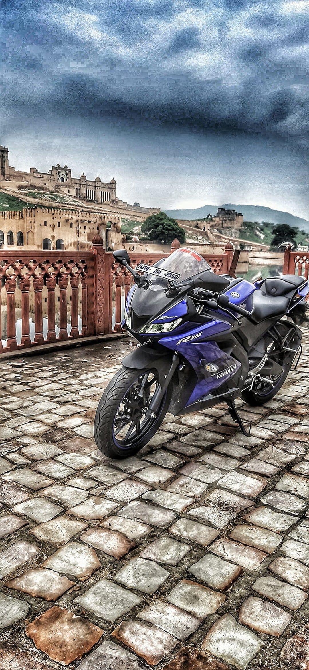 Blue Yamaha R15 motorcycle on a cobblestone path in front of the massive Amber Fort walls in Jaipur, India.