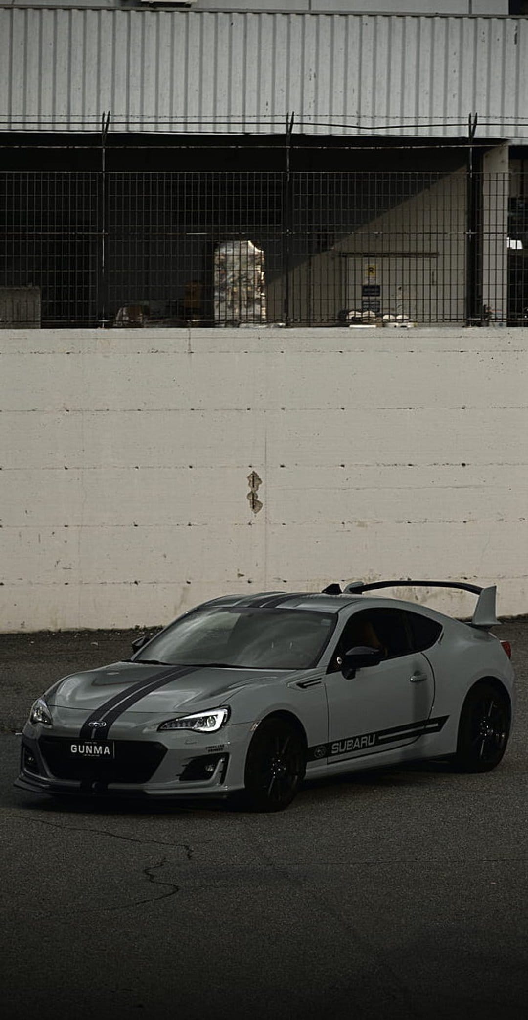 Subaru BRZ sports car with black racing stripes, large spoiler, and Gunma plates on an asphalt urban street.