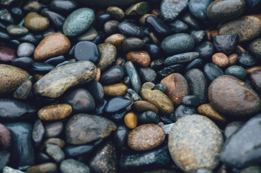 Smooth wet river rocks in shades of grey, brown, and green glisten with moisture in a tight macro composition.