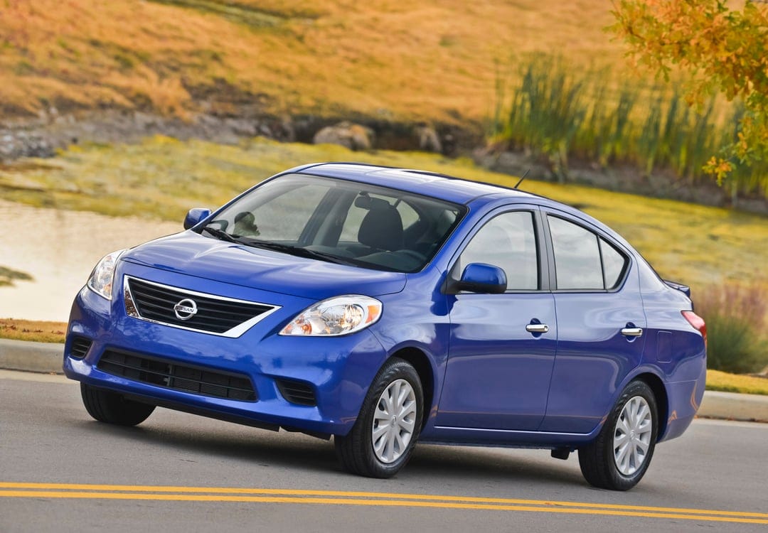 Blue Nissan sedan parked on a road with double yellow lines against a golden autumn hillside background.