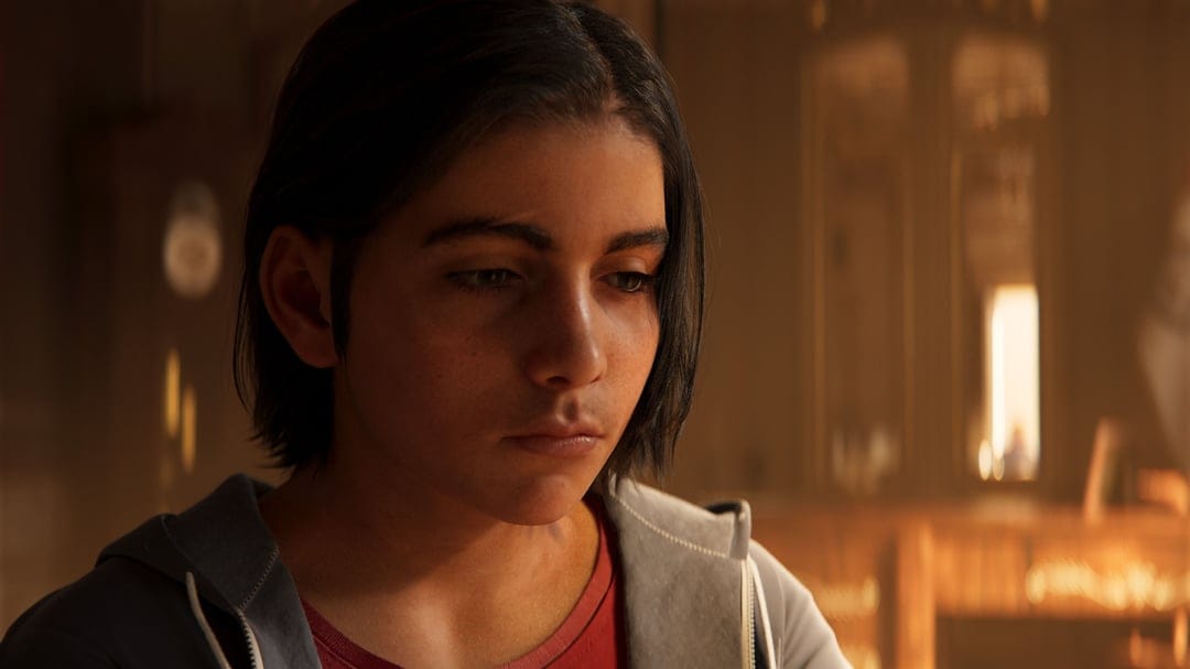 Young man with a somber expression looking down, illuminated by warm golden light in a blurred interior.