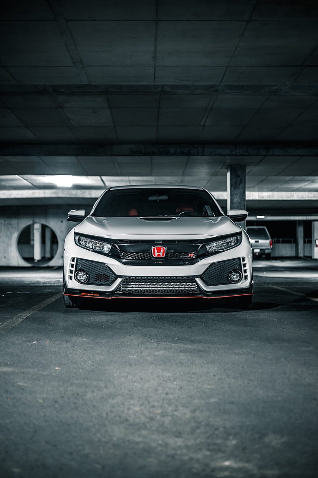 White Honda Civic Type R with red trim parked between concrete pillars in a dimly lit underground parking lot.