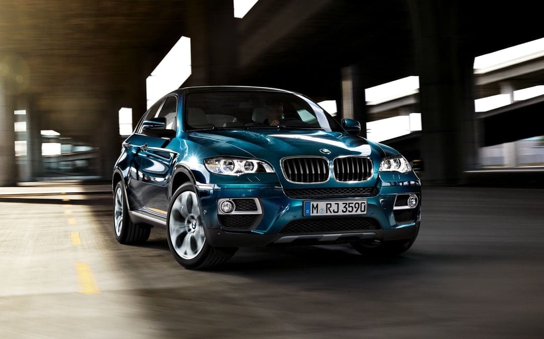 Deep blue BMW X6 luxury SUV driving through a dark concrete underpass with motion blur and sharp reflections.