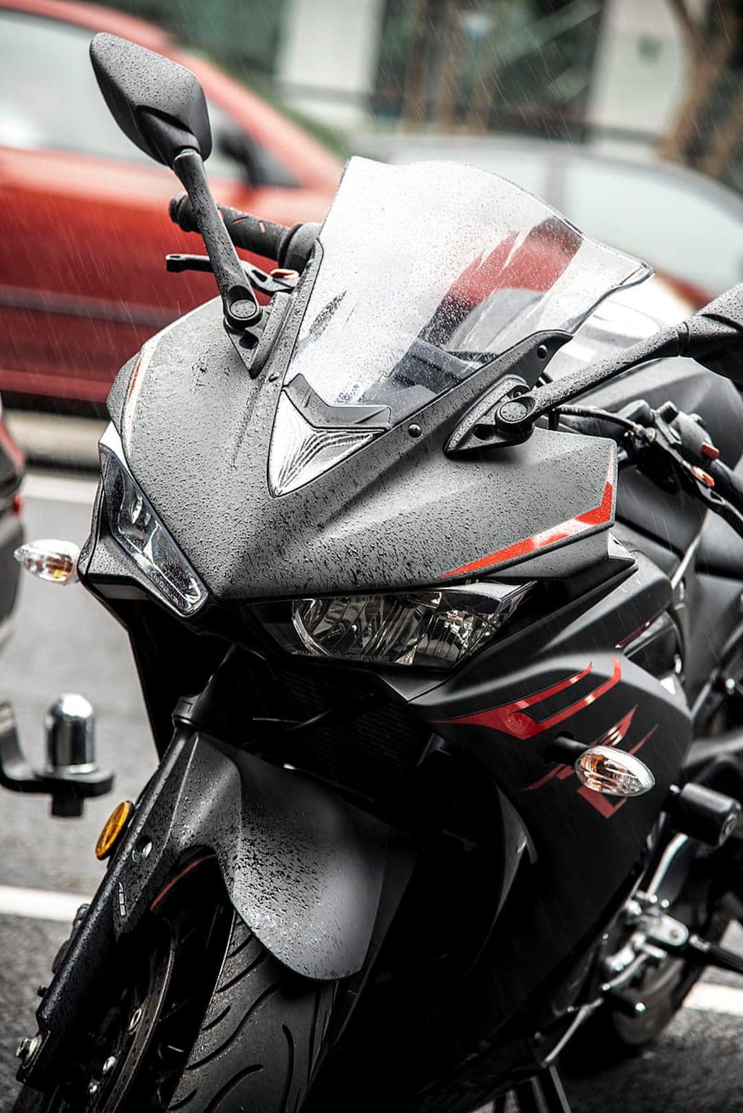 Black sport motorcycle with red trim covered in rain droplets, showcasing reflective metallic textures.