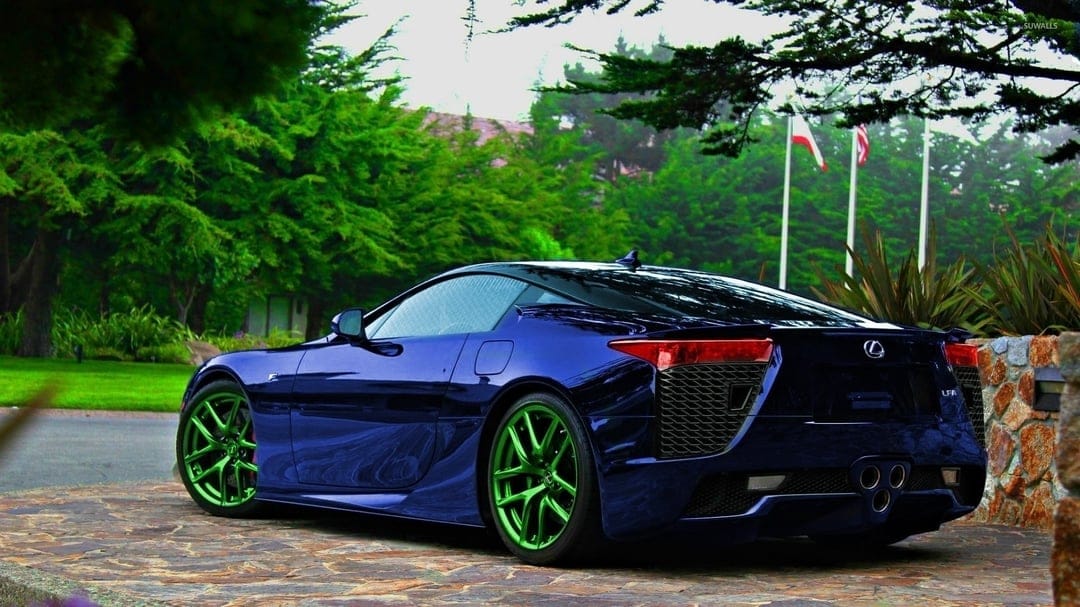 Blue Lexus LFA supercar with lime green rims on a stone driveway against a dense green forest background.
