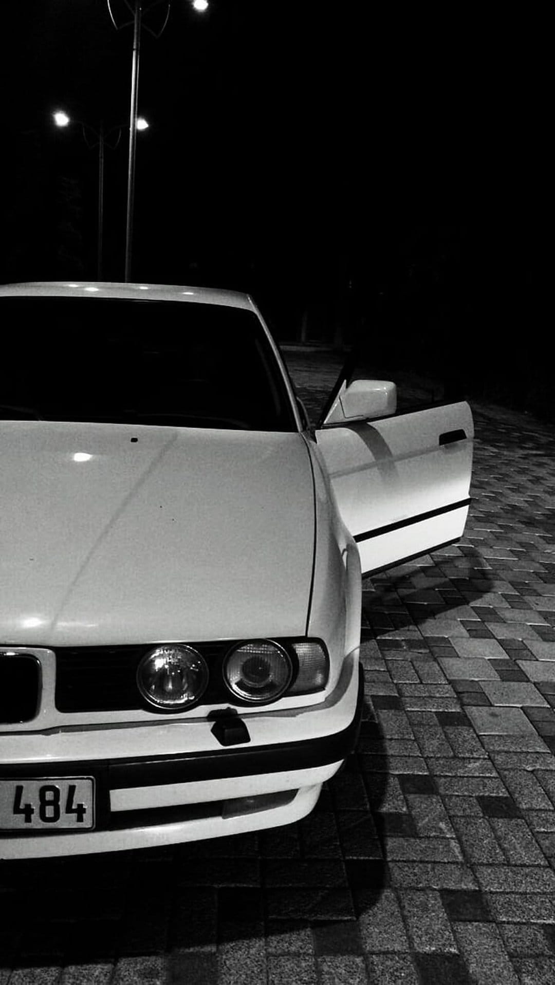 White vintage car with an open door parked on a dark street under bright lamps in high-contrast monochrome.