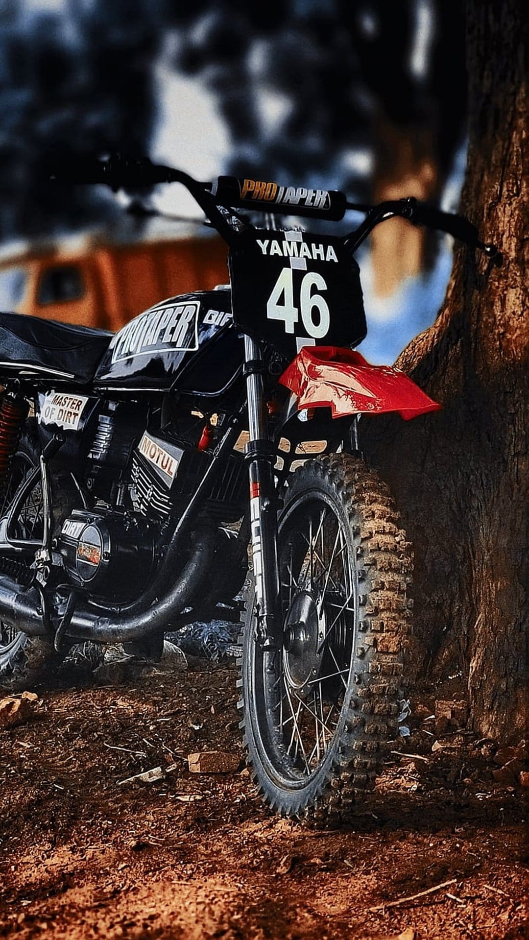 Yamaha dirt bike with number 46 and a red fender parked by a tree trunk, showing a knobby tire in close-up.
