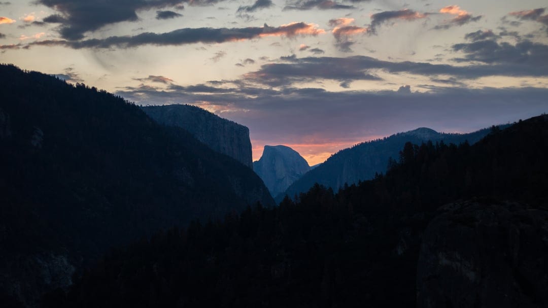 Half Dome granite peak silhouetted against a dramatic orange and purple sunset sky in Yosemite Valley.