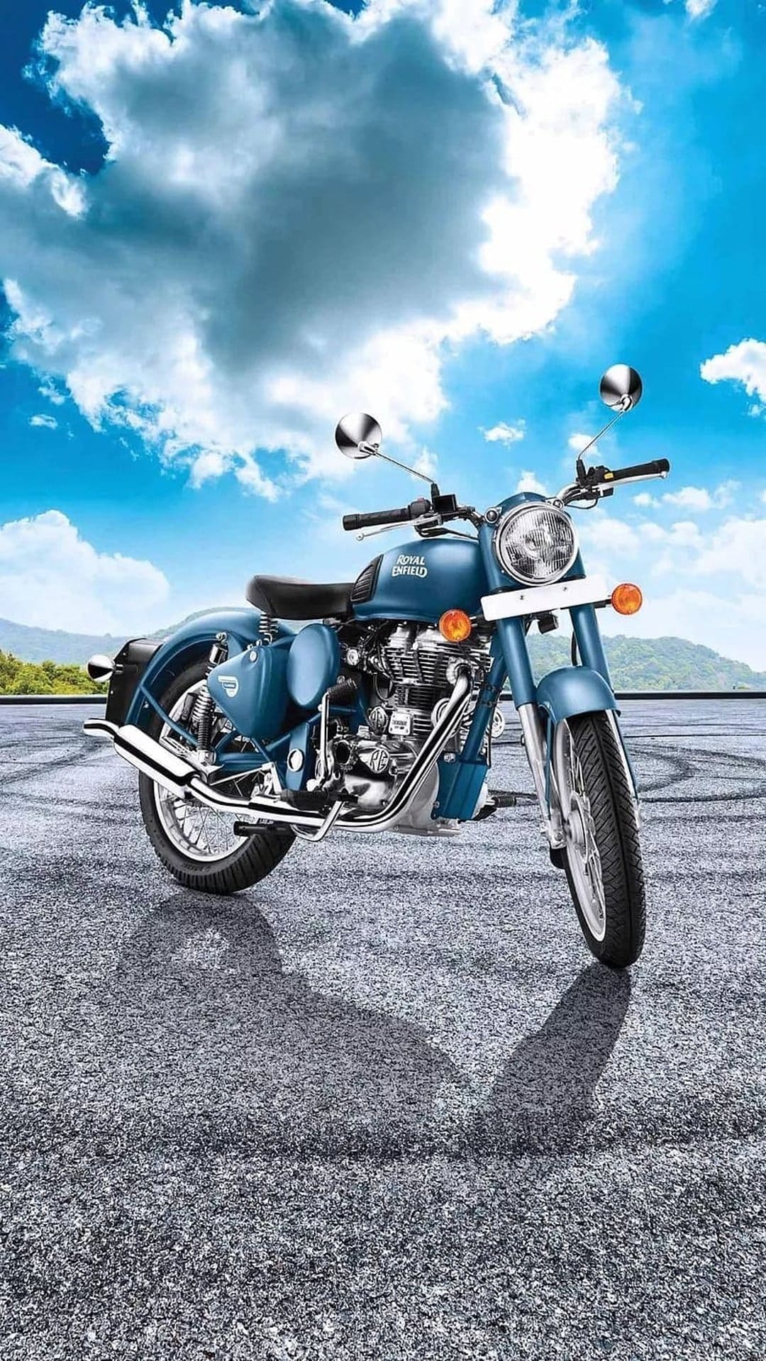 Blue Royal Enfield motorcycle with chrome accents on asphalt against a dramatic sky with distant hills.