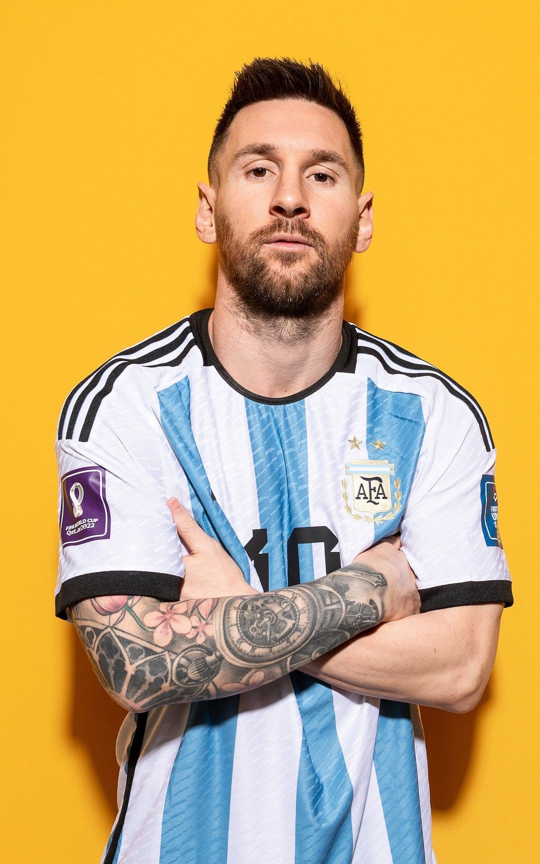 Lionel Messi stands with crossed arms wearing an Argentina jersey against a solid bright yellow background.