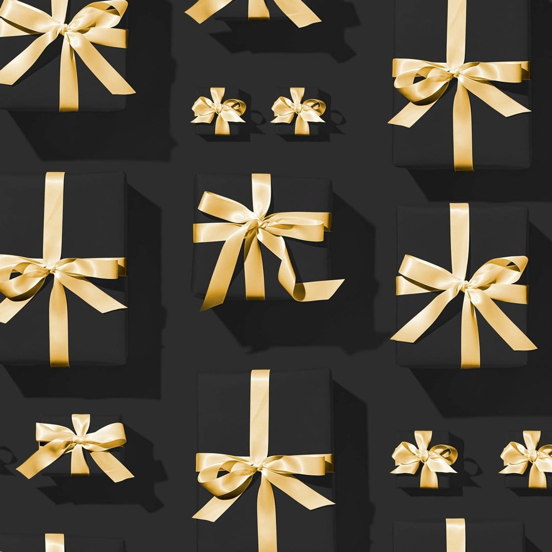 Matte black gift boxes with metallic gold bows create a repeating pattern across a dark textured surface.
