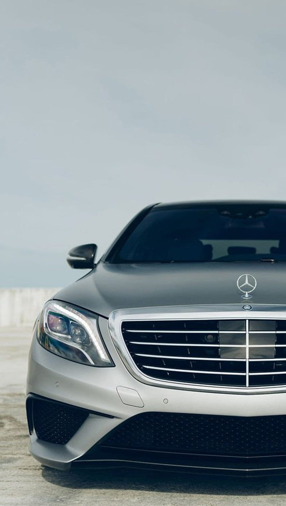 Silver Mercedes-Benz S-Class grille and sharp LED headlights under a soft, overcast sky in a close-up view.