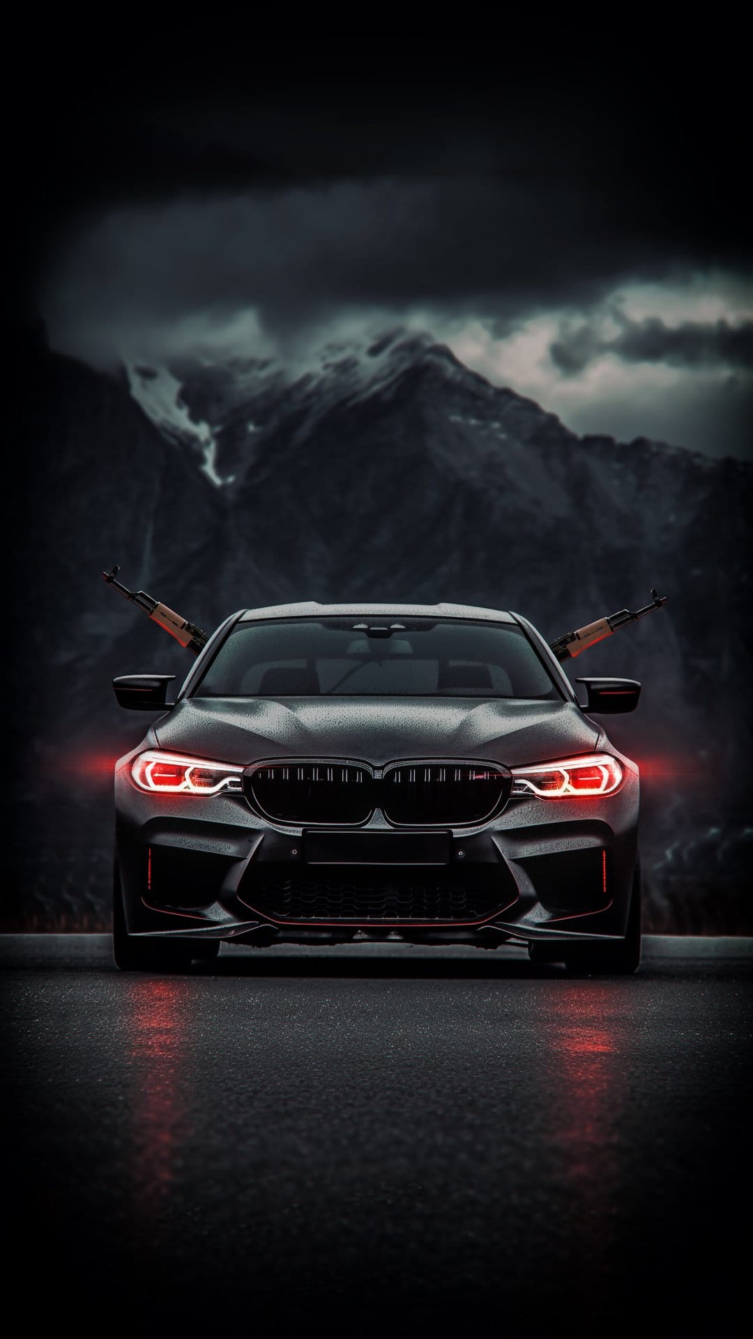 BMW M5 with red glowing headlights and rifles in the windshield parked on a wet road against cloudy mountains.