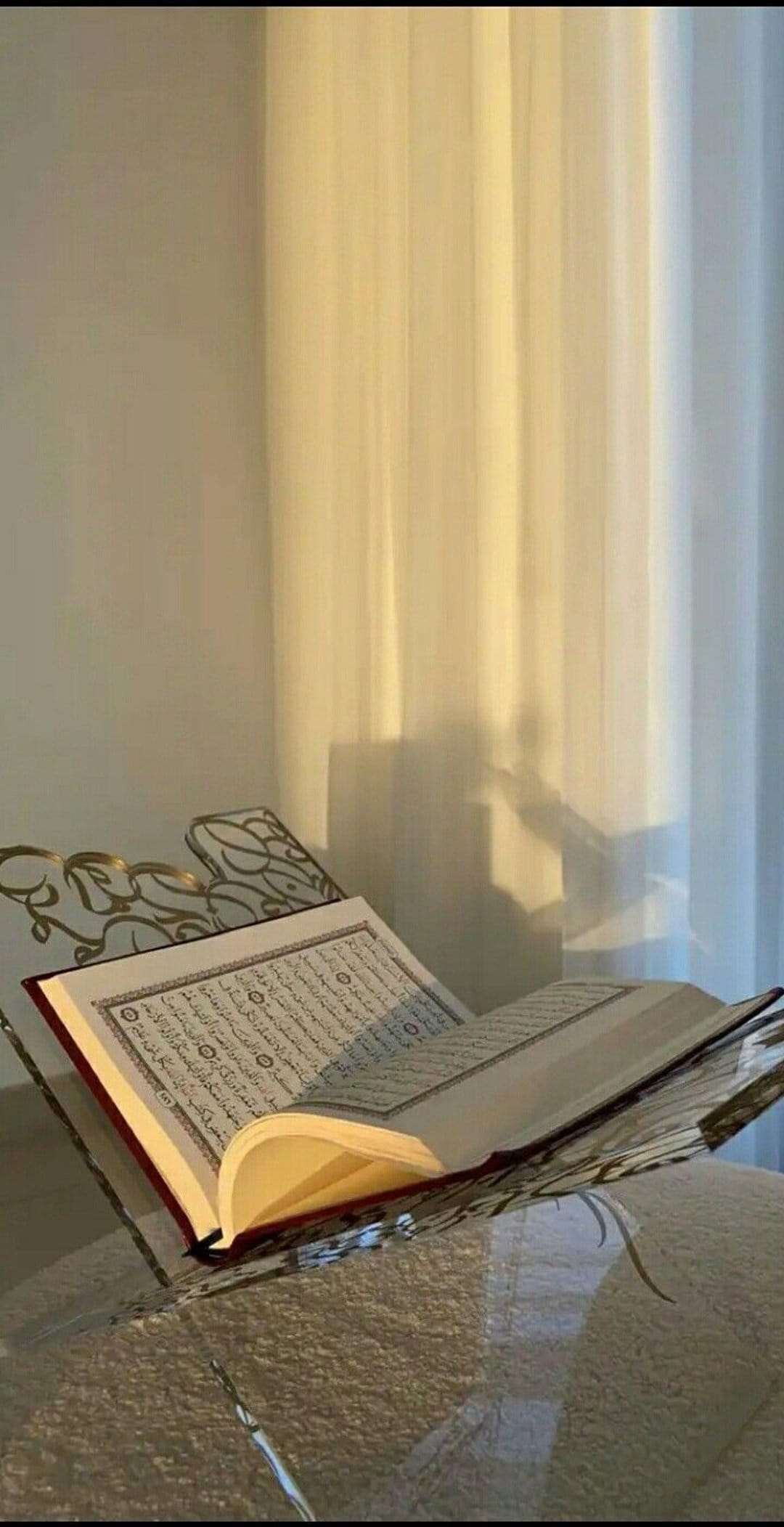 Open Quran resting on an ornate golden rehal stand, illuminated by soft window light and gentle shadows.