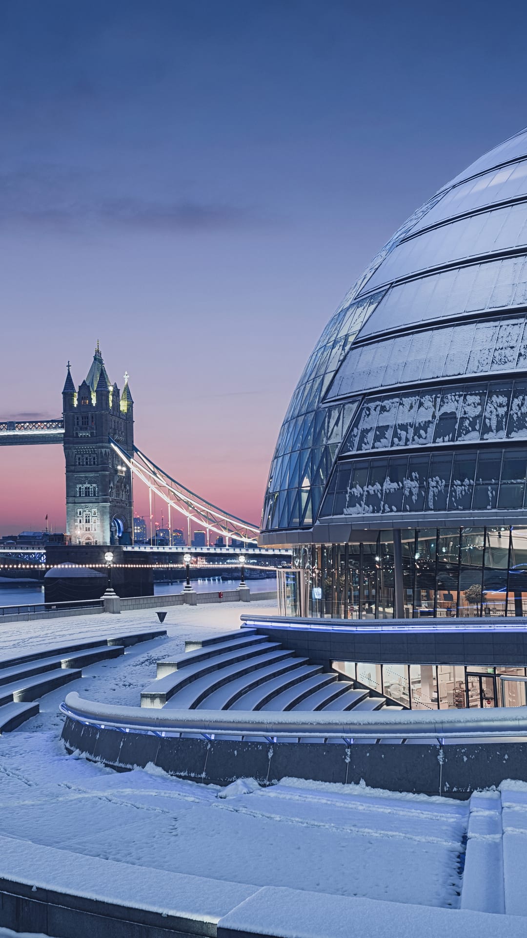 Tower Bridge and City Hall covered in snow during a pink twilight evening in London overlooking the Thames.