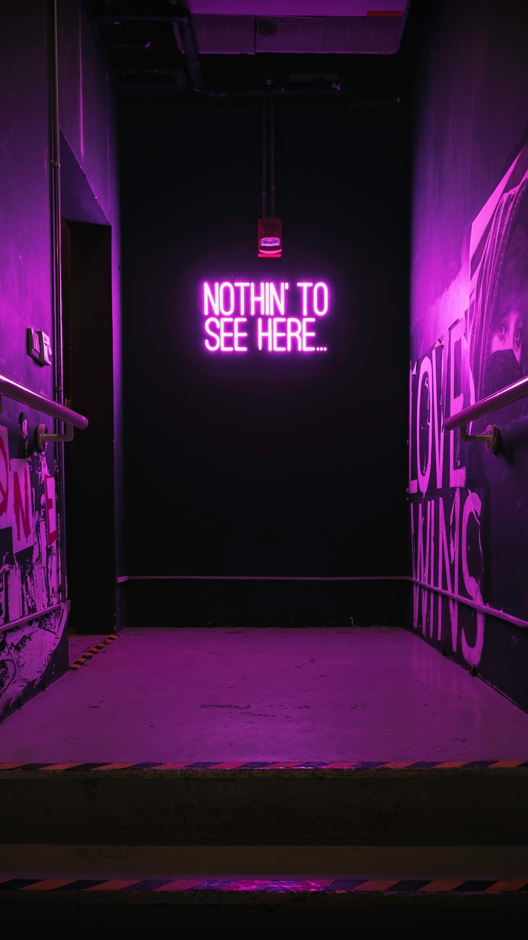 Purple neon sign with the text Nothin to See Here reflects on a dark alley floor in a moody urban scene.