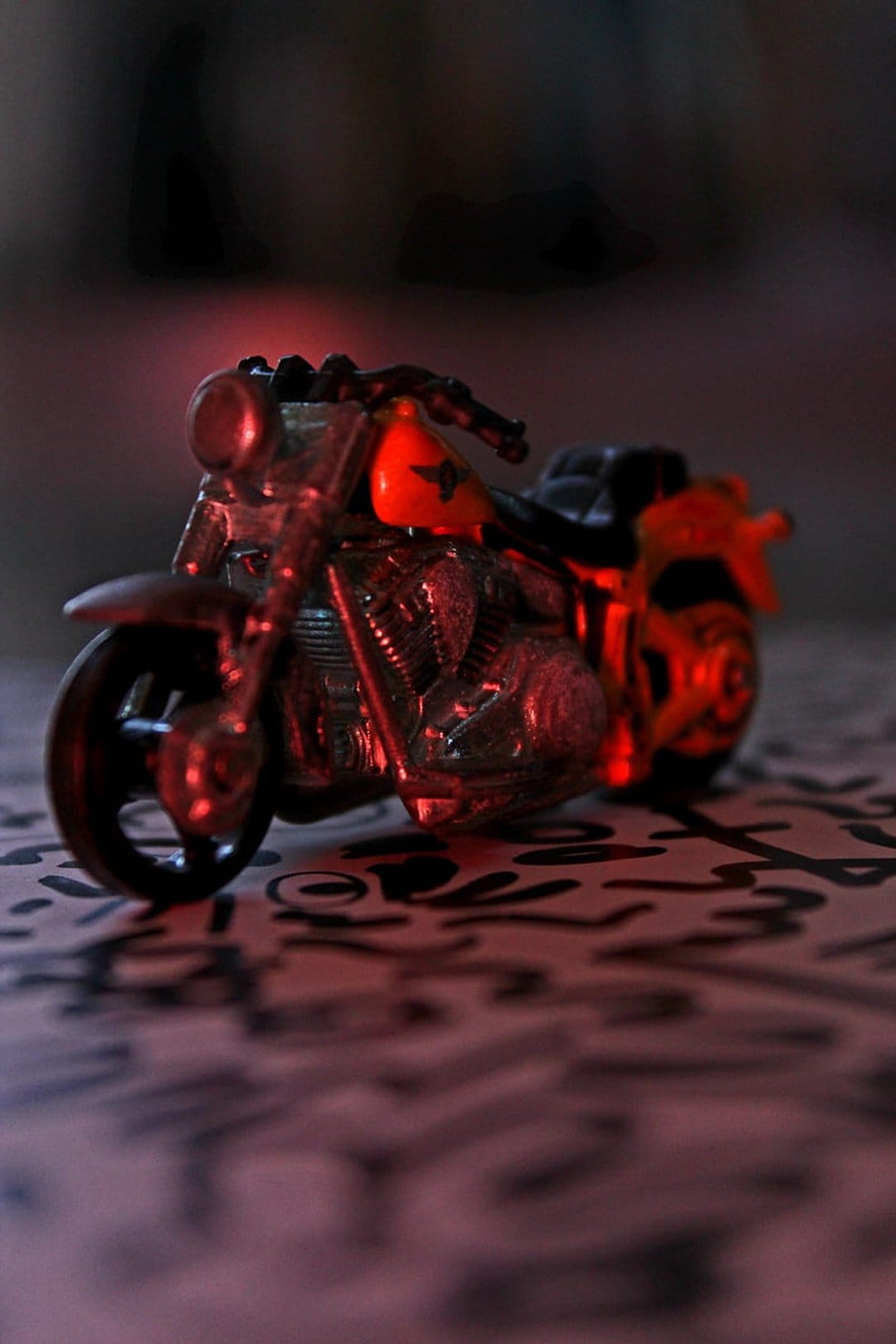Miniature motorcycle with an orange star tank and chrome engine glows under dramatic red light on a black surface.