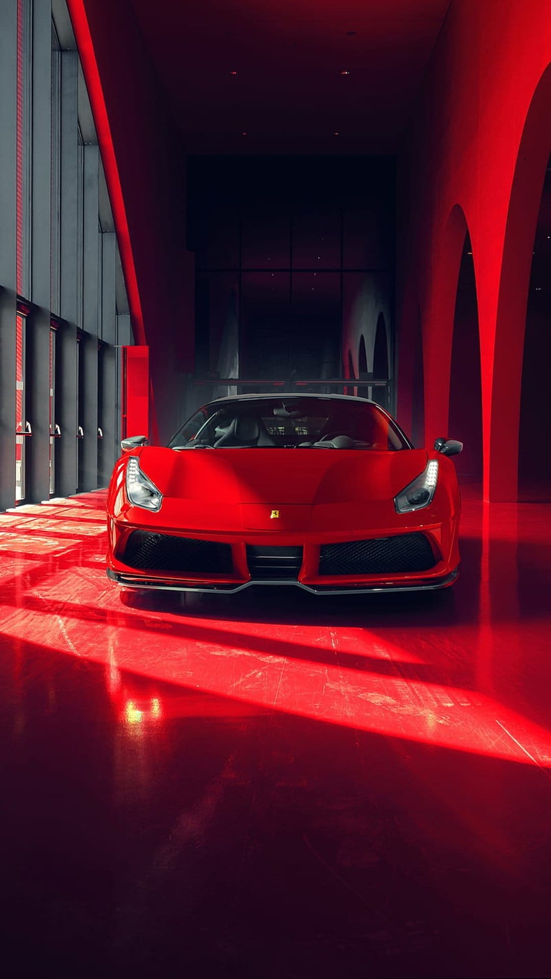 Red Ferrari sports car parked in a modern showroom with deep red walls, dramatic lighting, and floor shadows.