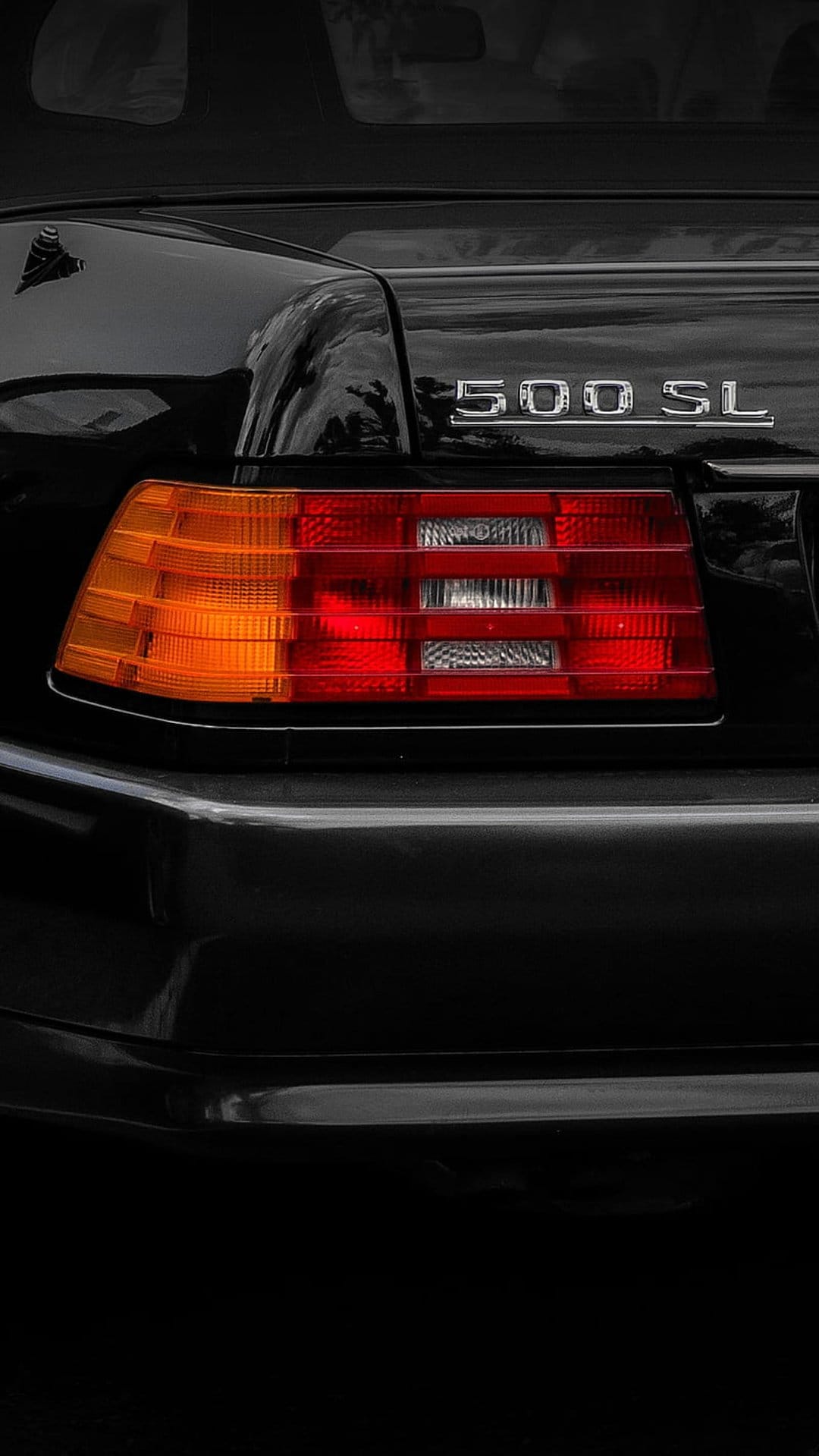 Mercedes-Benz 500 SL chrome badge and red ribbed taillight on polished black car paint with reflective highlights.