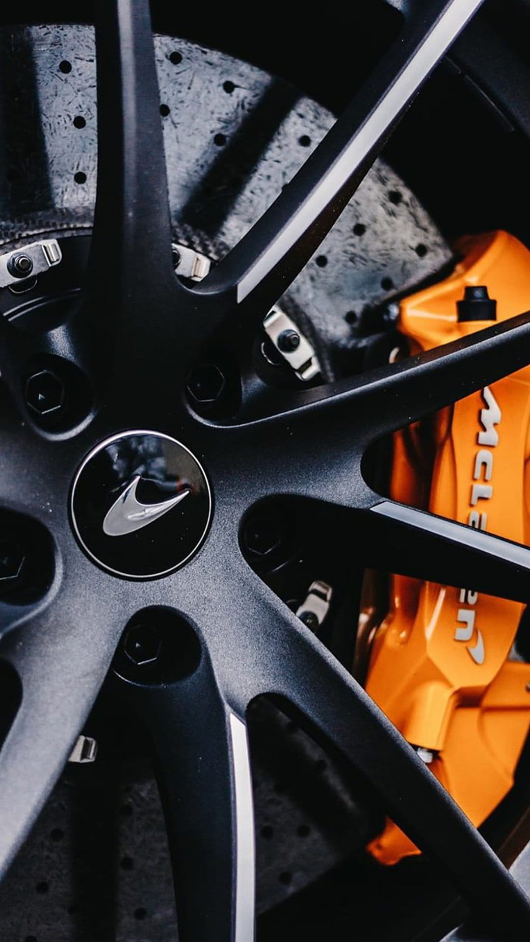 McLaren black alloy wheel featuring a bright orange brake caliper and silver logo on a ventilated metal rotor.