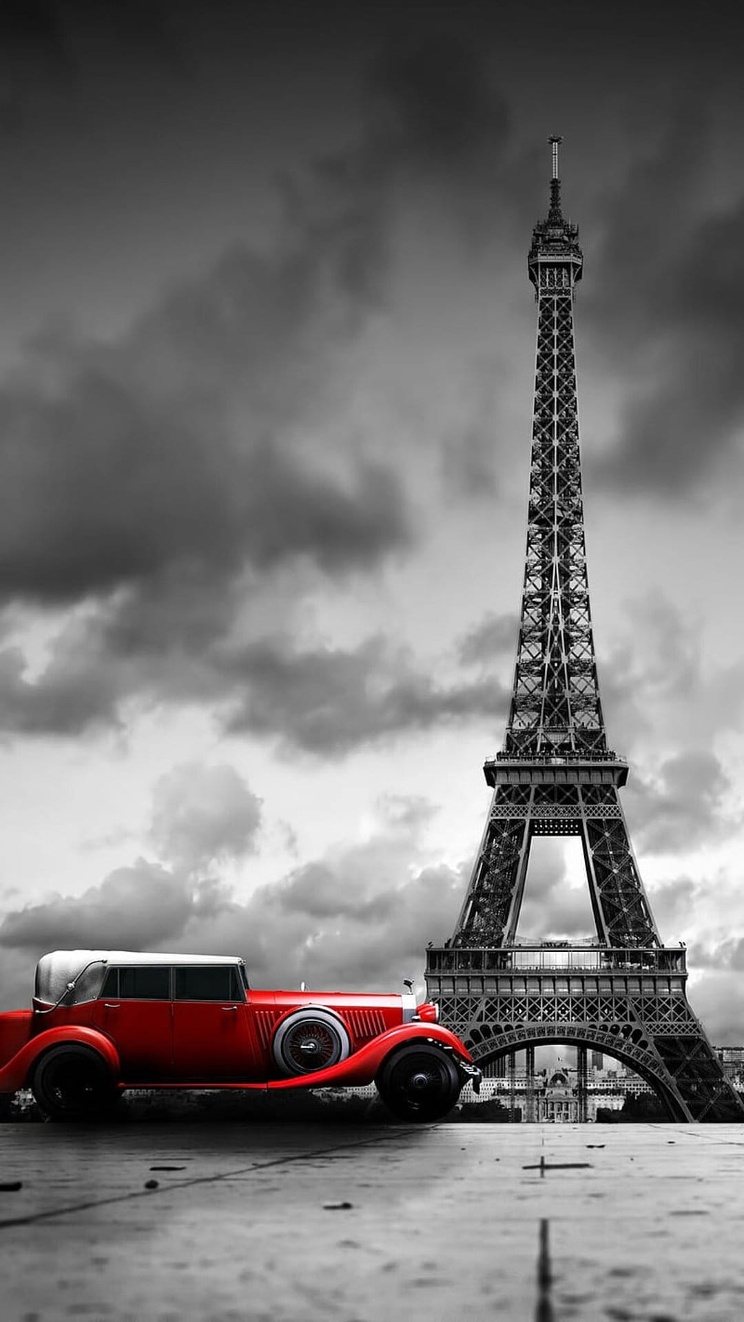Red vintage car parked on a Parisian street with the Eiffel Tower and a moody monochrome sky in the background.