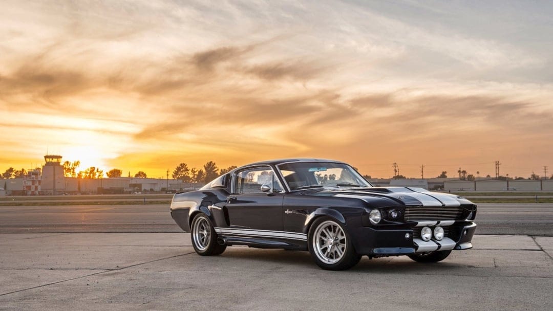 Midnight blue Shelby GT500 with white stripes on a tarmac under a golden sunset with a control tower.