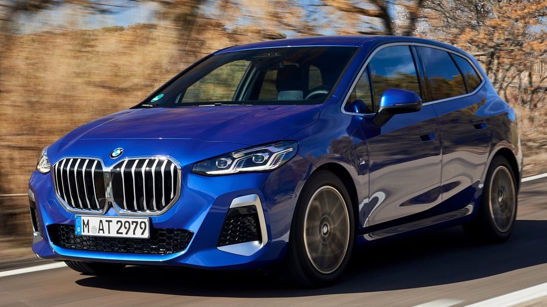 Blue BMW 2 Series Active Tourer driving fast on a sunlit road with a blurred autumn-toned landscape background.