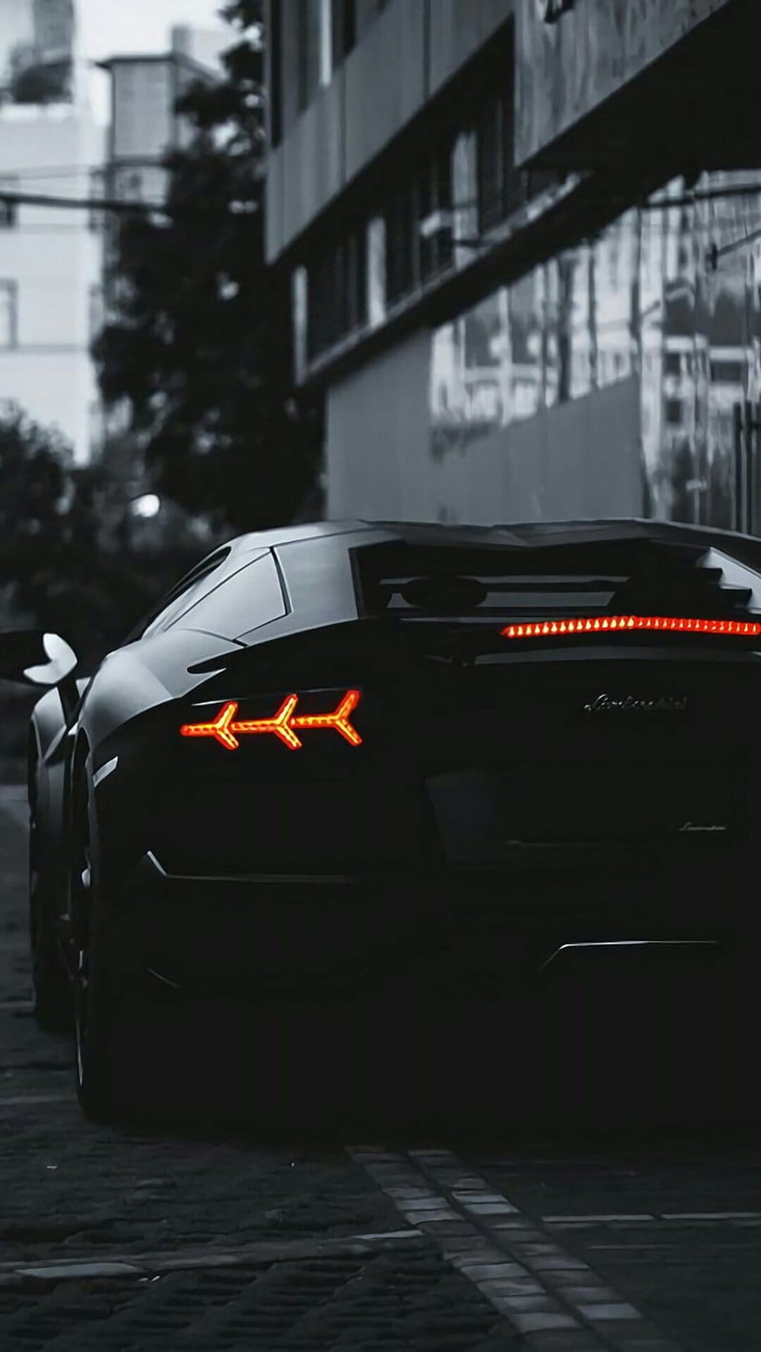 Black Lamborghini Aventador rear view with red Y-shaped taillights against a dark, gritty urban street at night.