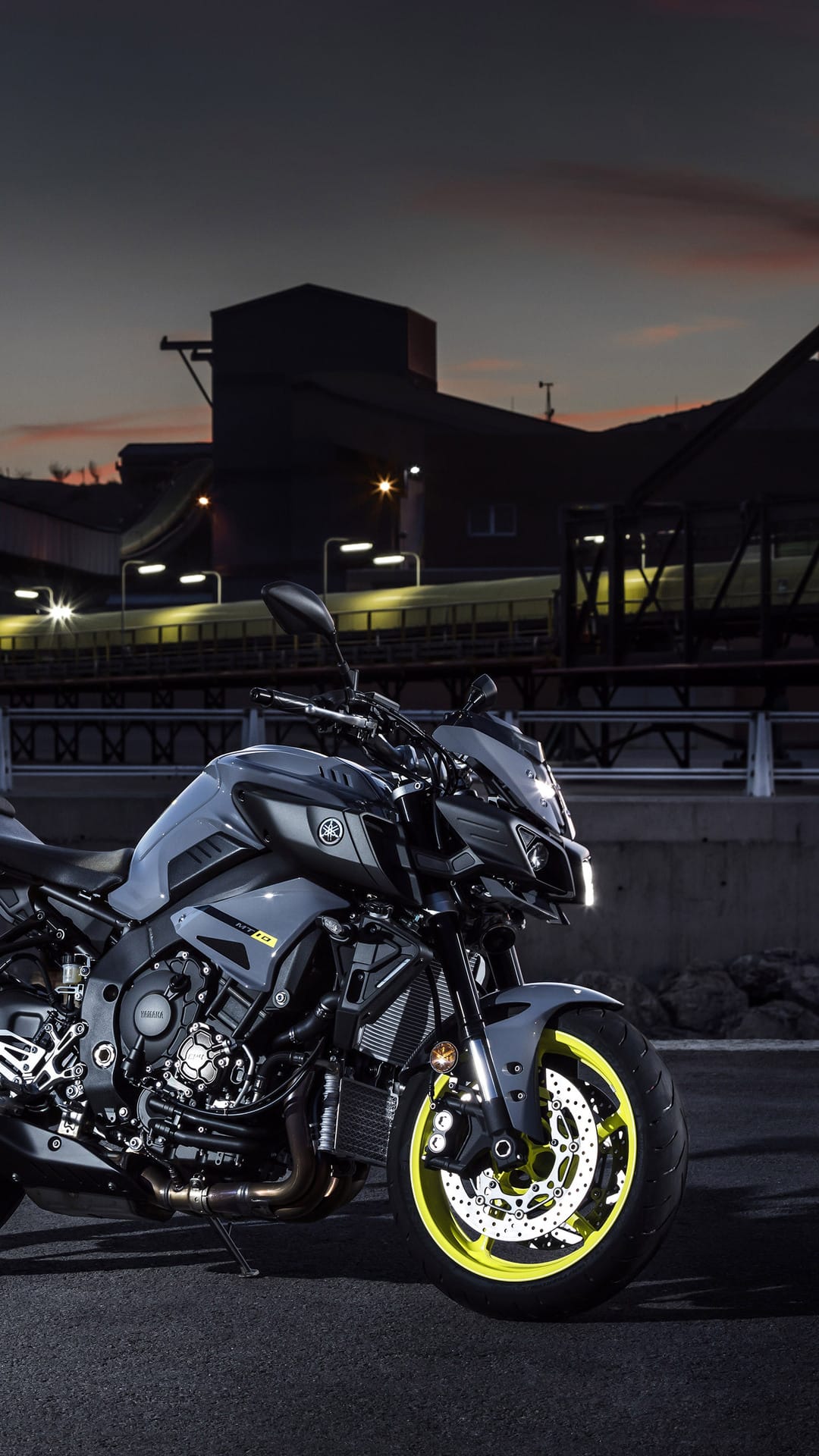 Yamaha MT-10 motorcycle with neon yellow wheels parked on asphalt against a lit industrial background at night.
