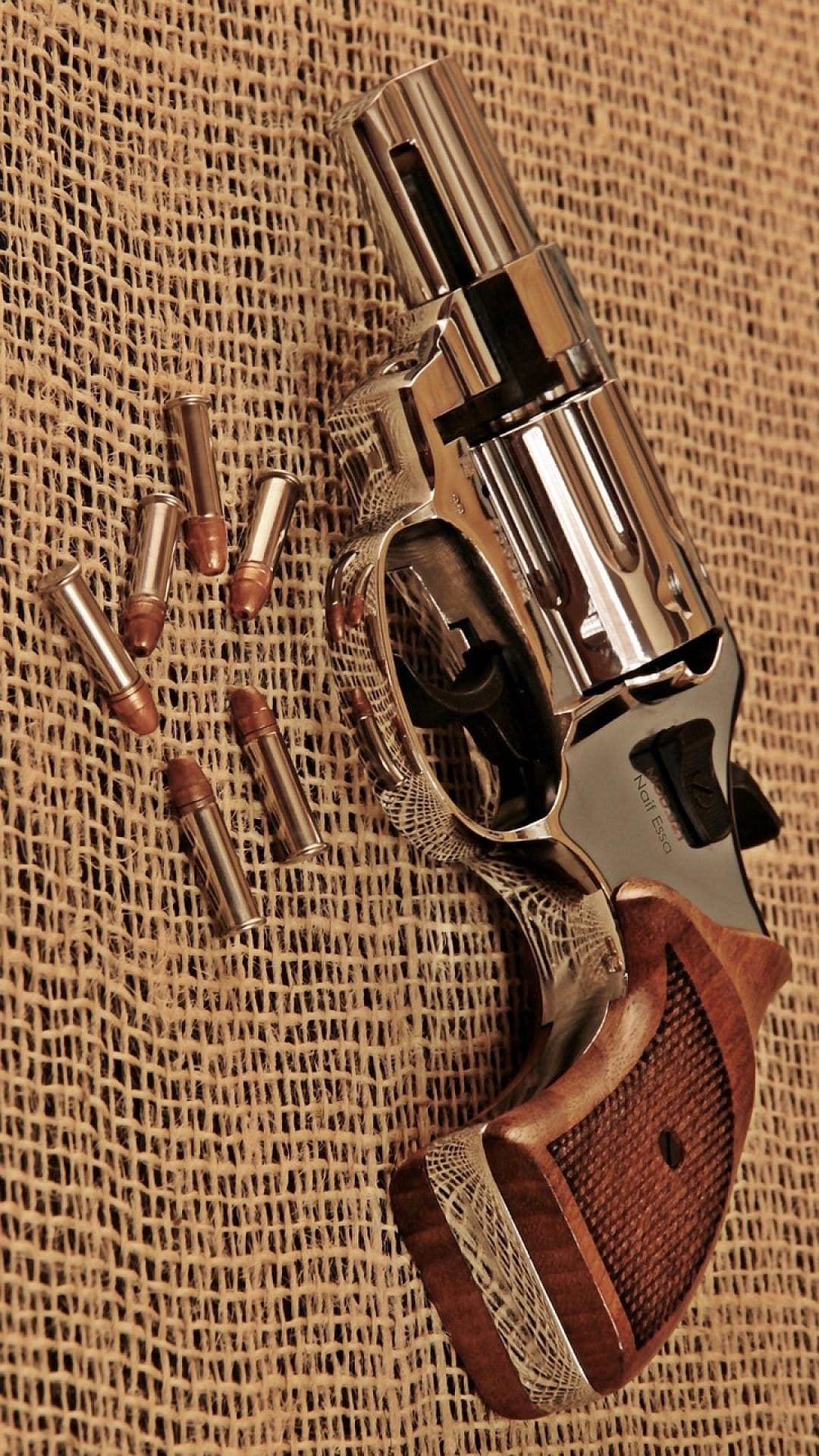 Chrome revolver with wood grips and brass bullets on a textured burlap background from a high-angle view.