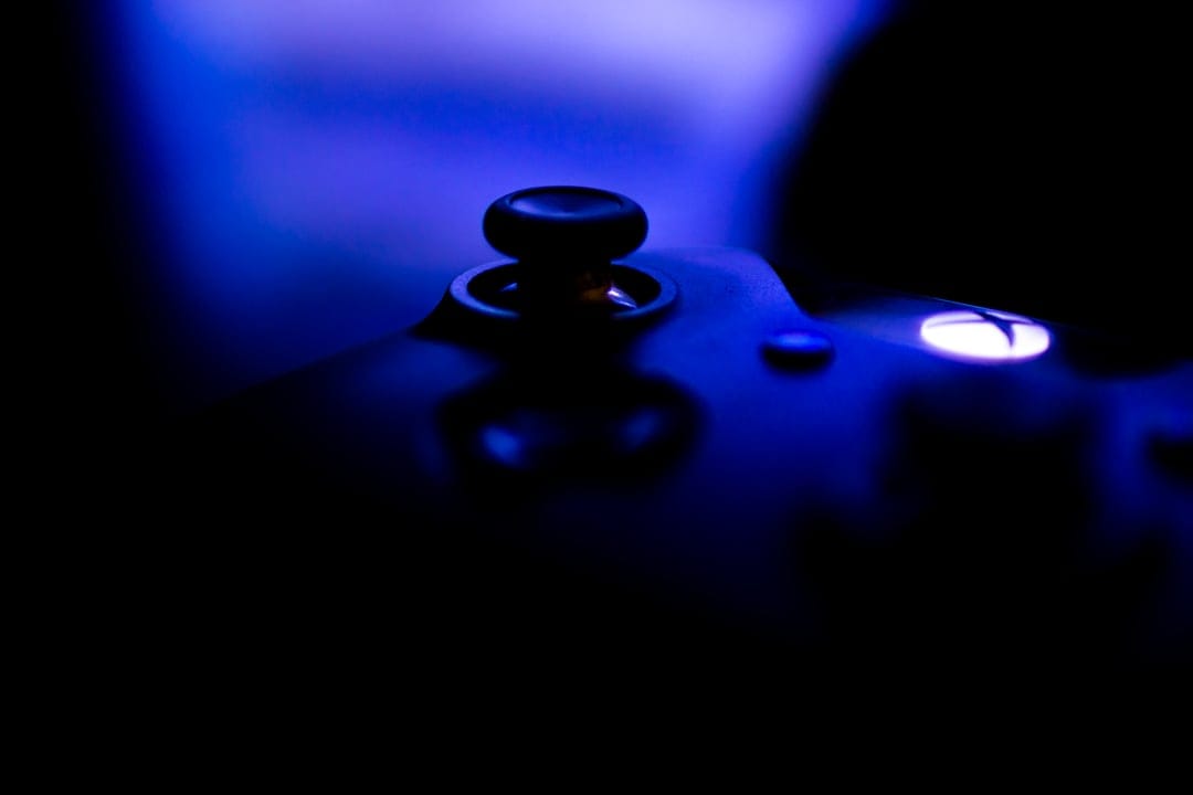 Black Xbox controller joystick and glowing white X button illuminated by a sharp, vibrant blue neon light.