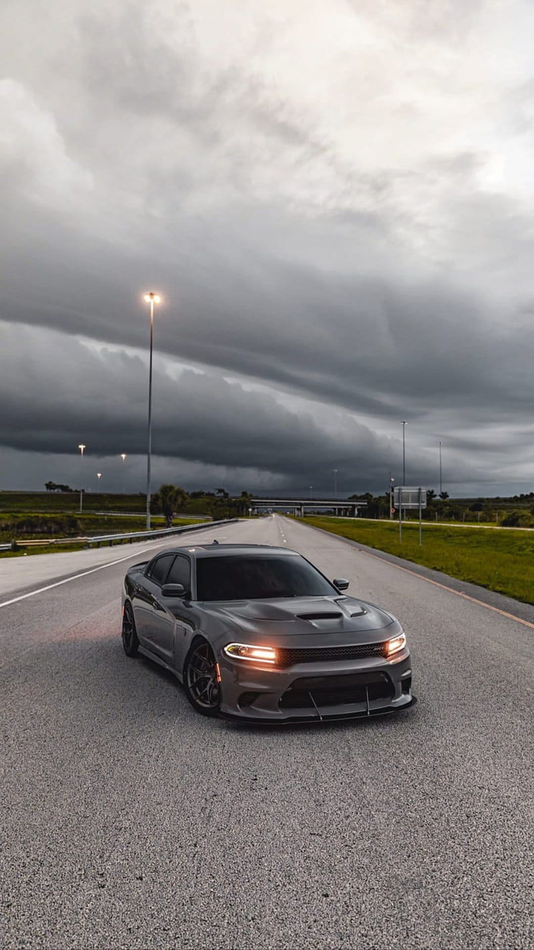 Dodge Charger on a dark highway beneath a heavy stormy sky with glowing headlights in a vertical view.