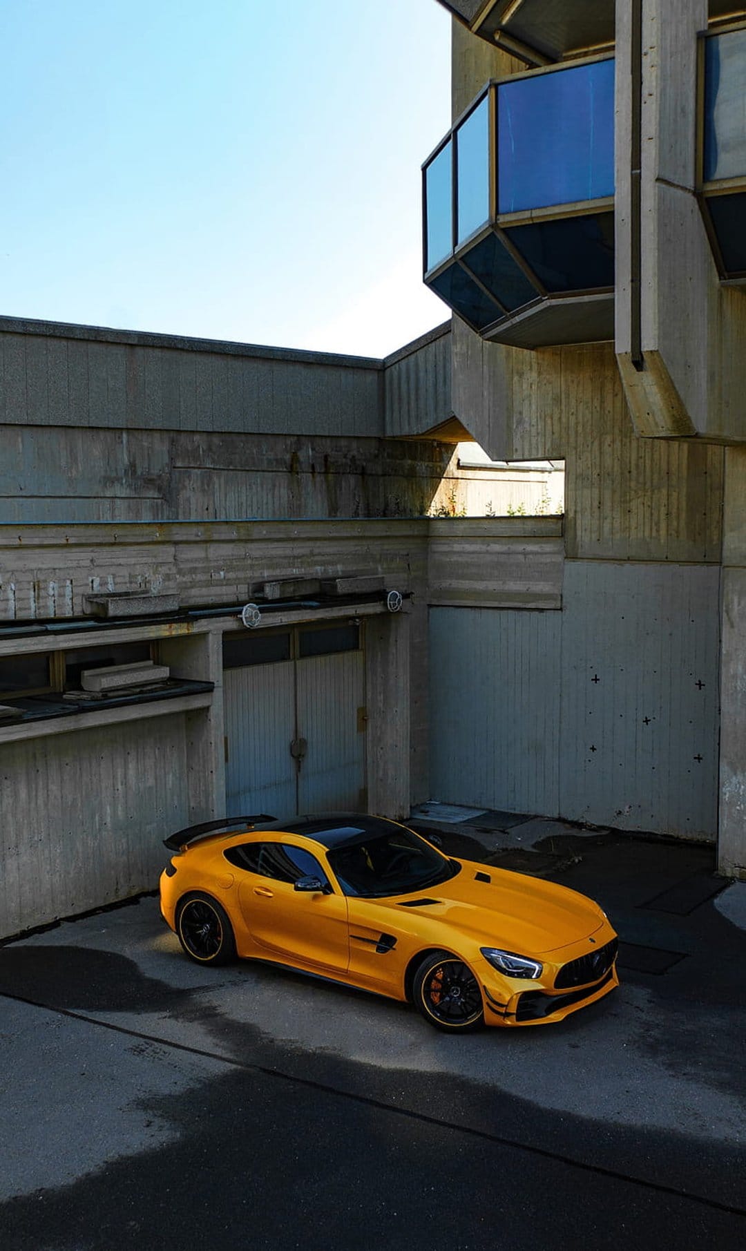Orange Mercedes-AMG GT R supercar angled against raw Brutalist concrete walls under bright afternoon sunlight.