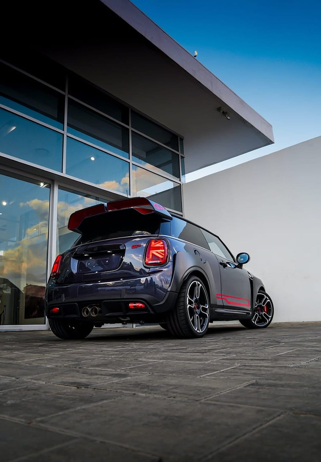 Mini Cooper JCW GP rear view featuring a red spoiler, dual exhausts, and blue sky reflections in glass.
