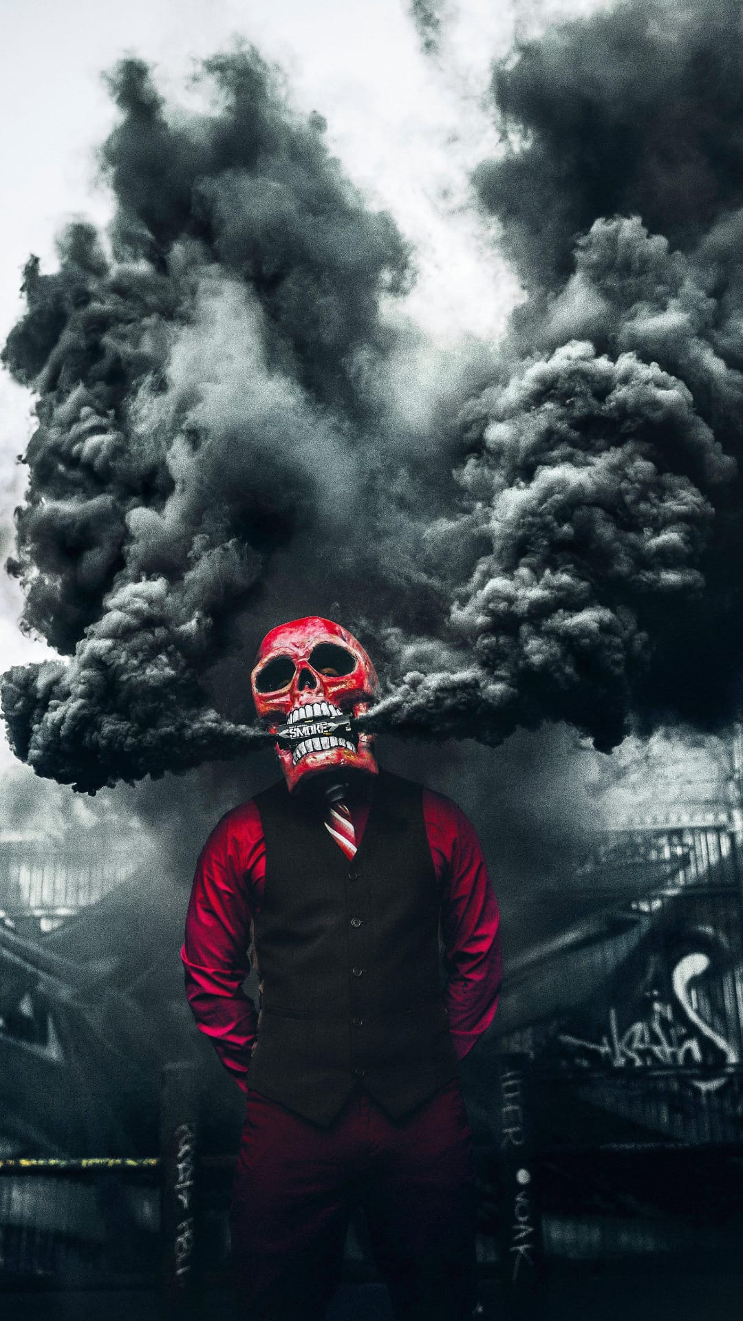 Red skull-masked man in a black vest exhales gray smoke amidst dark clouds and graffiti-covered city walls.