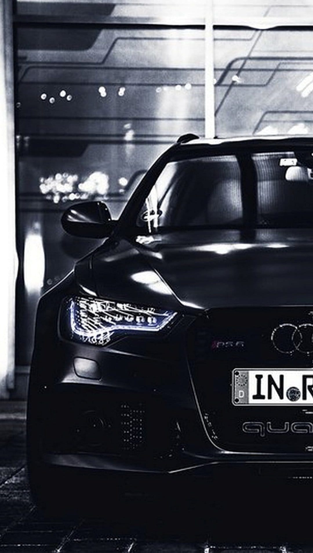Audi RS6 front grille and glowing LED headlights emerge from shadows against a textured modern wall.