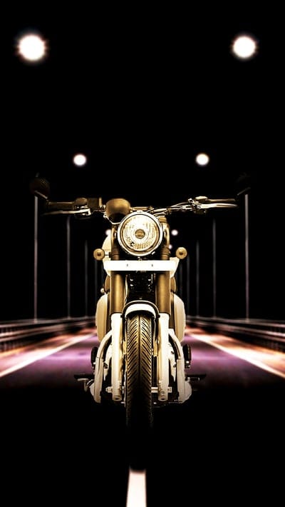 Classic motorcycle with a round headlight parked in a dark tunnel with purple and pink light reflections on the road.